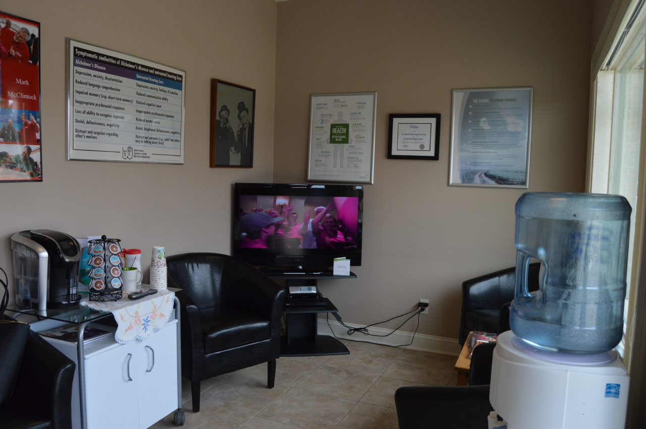 waiting room with chairs, tv, and coffee machine on table along with informational posters on walls