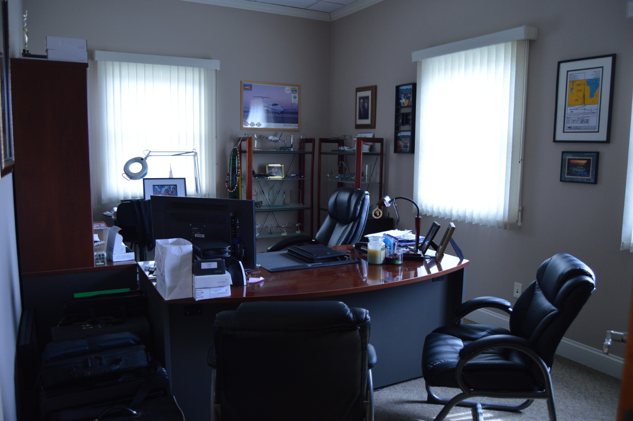 office with desk, chairs, and display in back with various awards and model planes